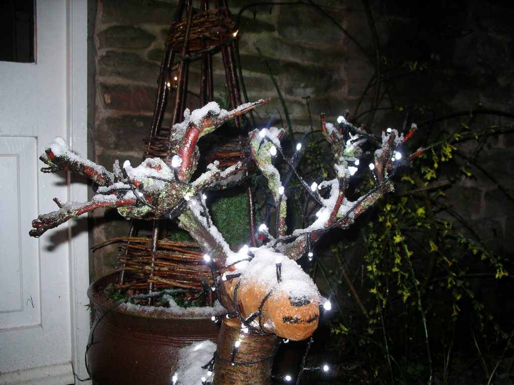 Wood reindeer decorated in Christmas lights, covered in snow